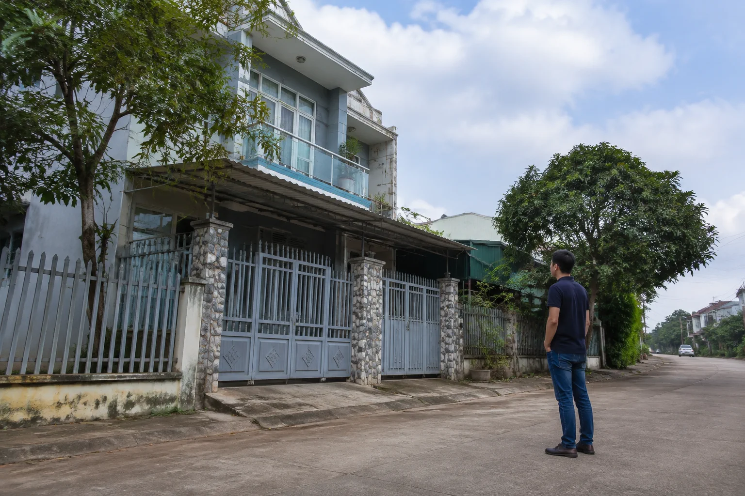 Người mua nhà đất tại Gia Nghĩa đứng trước một căn nhà phố địa phương, quan sát mặt tiền, lối vào và không gian xung quanh trong buổi khảo sát thực tế trước khi đặt câu hỏi với chủ