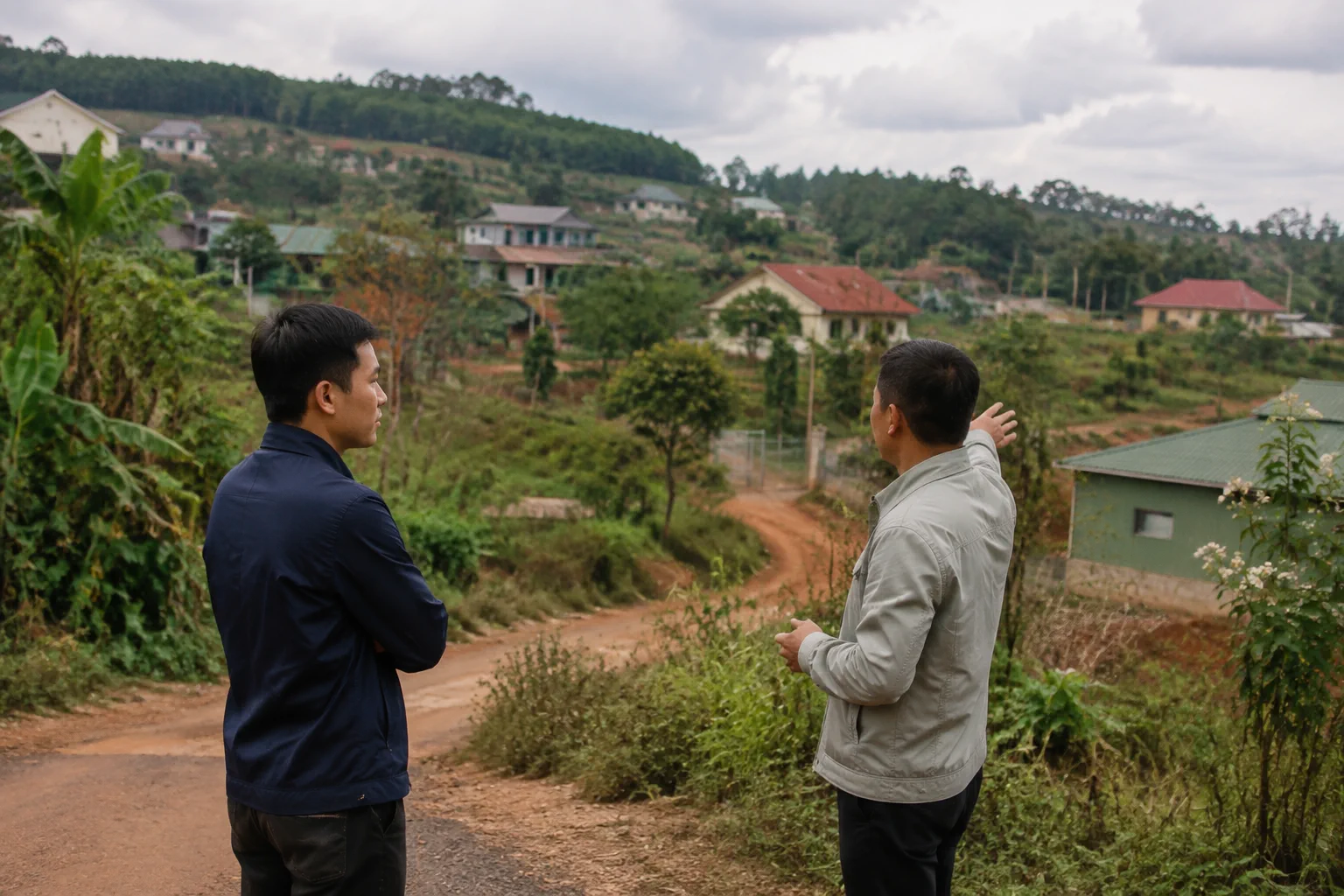 Người mua bất động sản đứng tại khu vực ven đất ở Đắk Nông quan sát vị trí thửa đất và trao đổi thông tin ban đầu trước khi kiểm tra, thể hiện bước chuẩn bị dữ liệu về tài sản thay