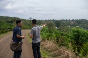 Toàn cảnh một nhà đầu tư ở xa đang trao đổi nhu cầu tìm kiếm bất động sản Đắk Nông với người tư vấn địa phương tại một không gian mở gần khu vực nông thôn, hai người cùng quan sát